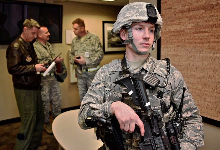 Airman Dylan Crosby, 375th Air Mobility Wing Security Forces team member, stands ready as entry controller, at the 932nd Airlift Wing headquarters building, during an active shooter exercise, Mar. 4, 2017, Scott Air Force Base, Illinois.   In the background, the 932nd AW Director of Inspections, Lt. Col. Ralph DePalma (leather jacket), and members of the Wing Inspection Team, or WIT, discuss final steps as the exercise is called to an end and normal actives resumed.   Crosby, who was on patrol, said they responded fast and got to the threat quickly.   (U.S. Air Force photo by Tech. Sgt. Christopher Parr)