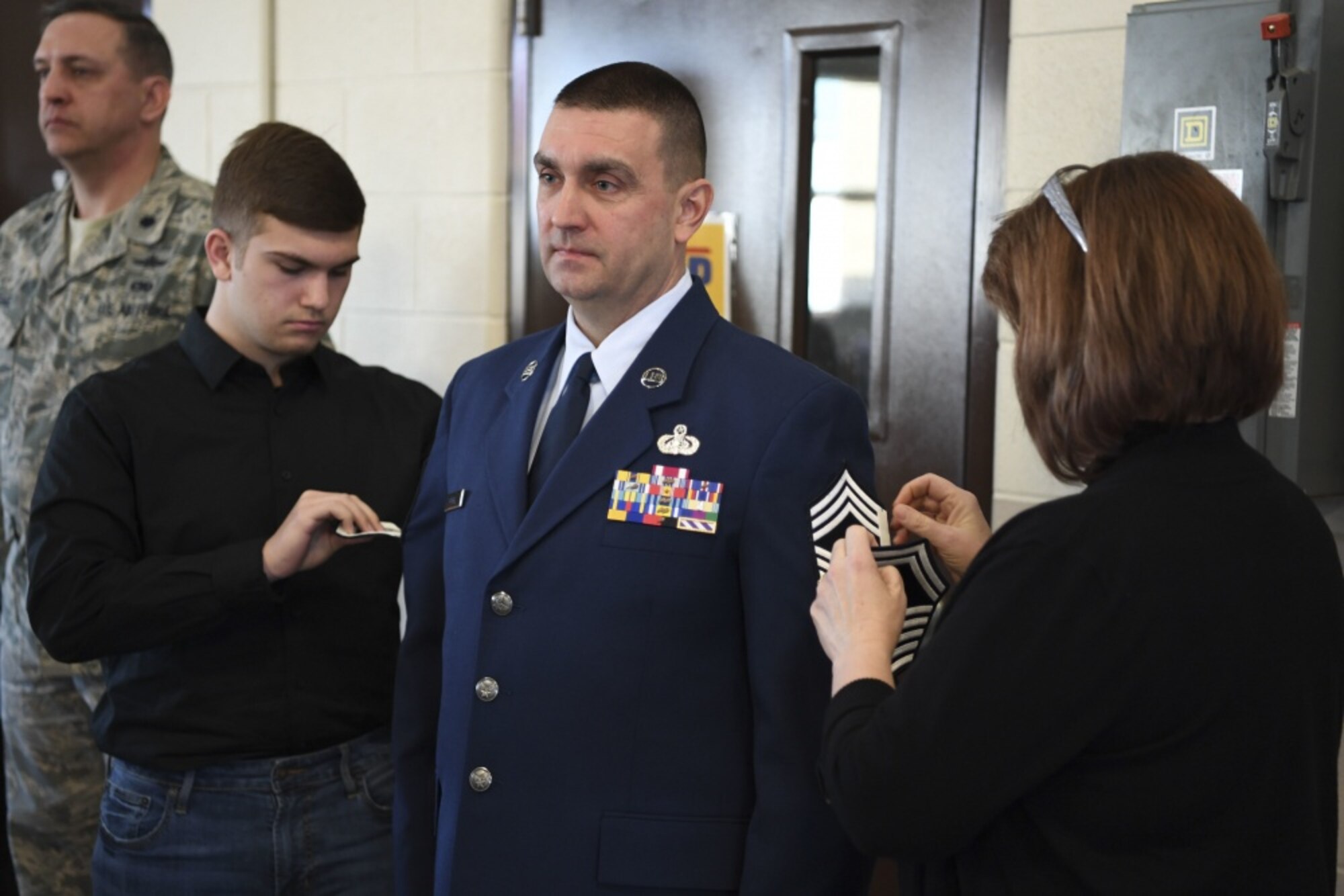 Chief Master Sgt. Mike Powell, 130th Airlift Wing communications flight chief enlisted manager, stands at attention while members of his family pin on his new rank of chief master sergeant March 4, 2017 at McLaughlin Air National Guard Base, W.Va. Powell was promoted to the enlisted corps' highest rank during a formal promotion ceremony held in his honor. (U.S. Air National Guard photo by Tech. Sgt. Eugene Crist.) 
