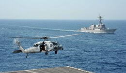 An MH-60S Sea Hawk helicopter attached to the Dragon Whales of Helicopter Sea Combat Squadron (HSC) 28 drops supplies on the flight deck of the aircraft carrier USS George H.W. Bush (CVN 77) during a vertical replenishment. The guided-missile destroyer USS Truxton (DDG 103) is in the background. George H.W. Bush is supporting maritime security operations and theater security cooperation efforts in the U.S. 5th Fleet area of operations. (U.S. Navy photo by Mass Communication Specialist 3rd Class Margaret Keith/Released)