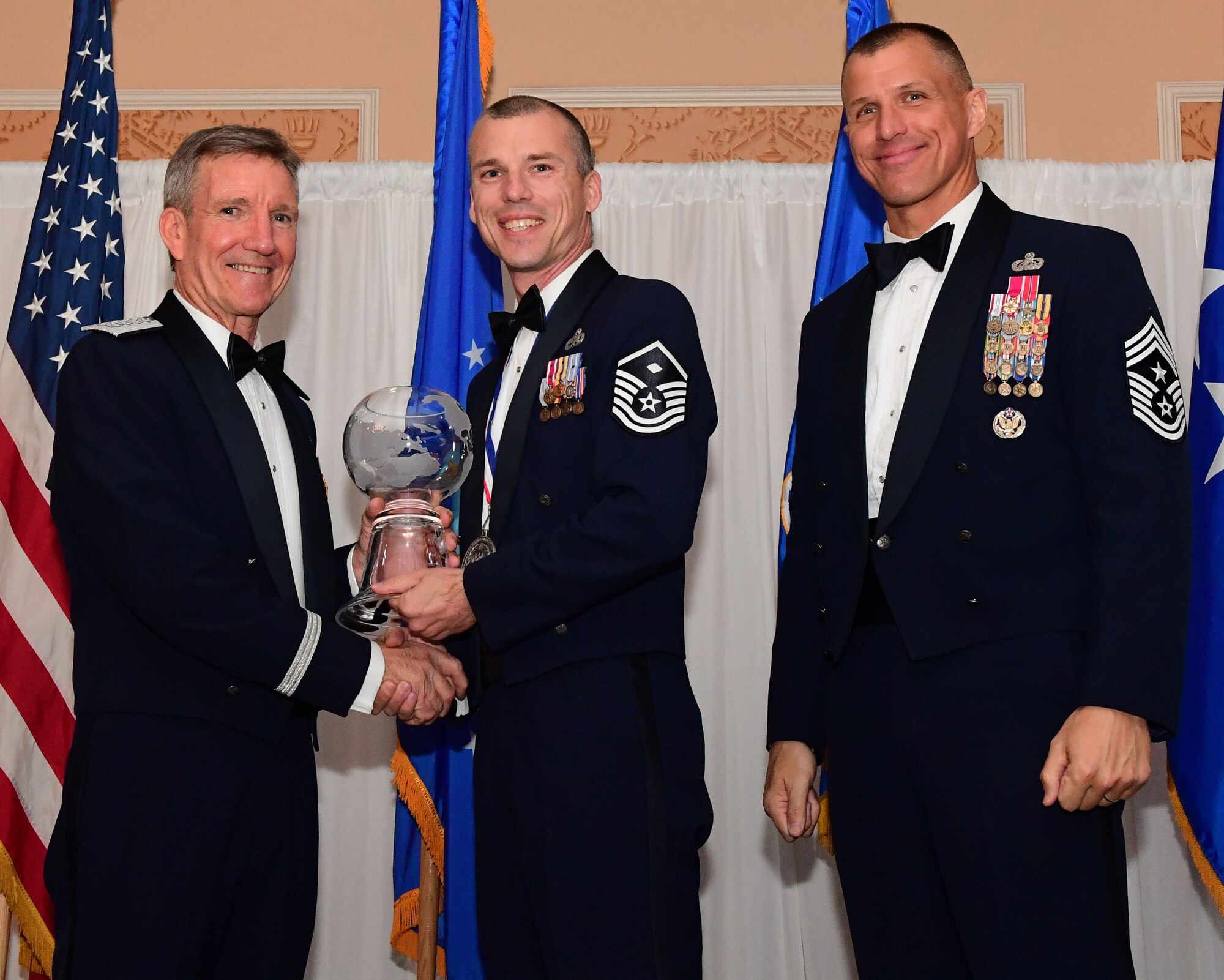 Gen. Hawk Carlisle, left, commander, Air Combat command presents an award to Master Sgt. Mark Curtis, 379th Expeditionary Aircraft Maintenance Squadron first sergeant, as Chief Master Sgt. Steve McDonald, command chief, ACC observes during the 2017 Outstanding Airmen of the Year banquet at the Bayview Community Center in Langley AFB, Virginia, March 8, 2017. The 12 Outstanding Airmen earn the Outstanding Airman ribbon with the bronze service star device and wear the Outstanding Airman badge for one year. They also serve on the Air Force Enlisted Council for one year. (U.S. Air Force photo by Staff Sgt. Nick Wilson)