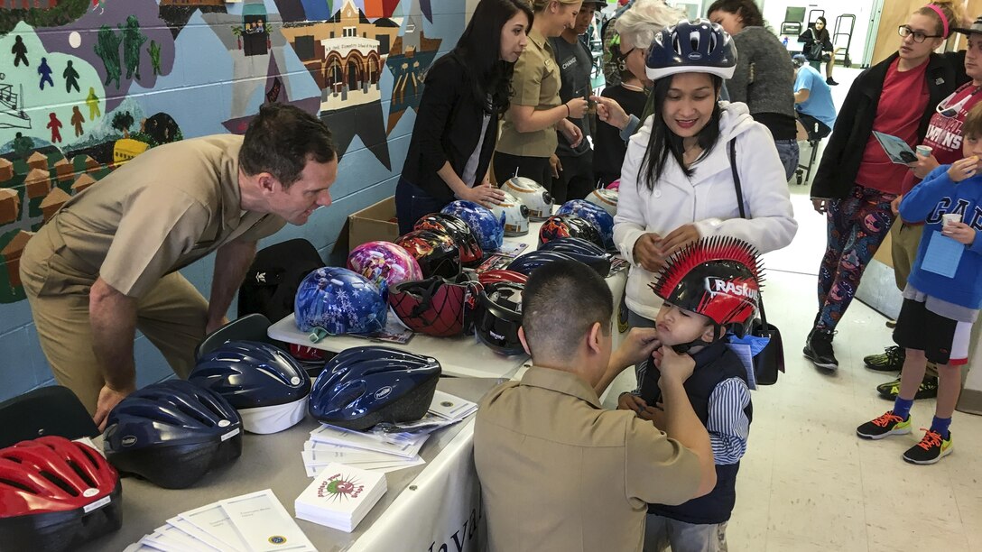 Navy Lt. Joseph Cahill, a neurologist at Naval Hospital Pensacola, observes the fit of a helmet on Ron Jay, 5, at an elementary school in Pensacola, Fla., March 4, 2017. Sailors from the hospital's neurology department and graduate students from a local behavioral medicine clinic visited  the school to promote helmet safety to children and their parents. Navy photo