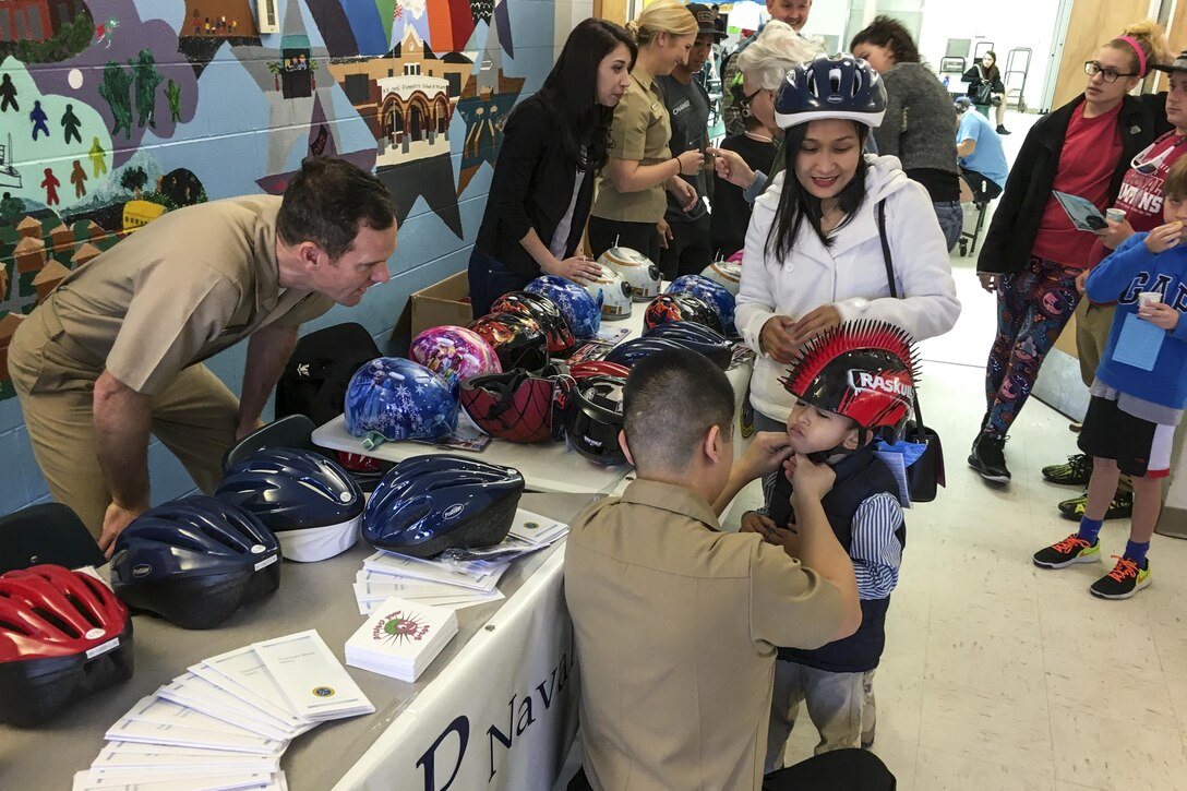 Navy Lt. Joseph Cahill, neurologist at Naval Hospital Pensacola, observes the fit of a helmet on Ron Jay, 5, at an elementary school in Pensacola, Fla., March 4, 2017. Sailors from the hospital's neurology department and graduate students from a local behavioral medicine clinic visited  the school to promote helmet safety to children and their parents. Navy photo