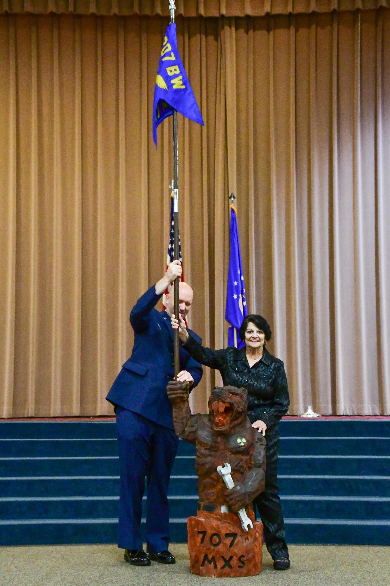 U.S. Air Force Senior Master Sgt. Frank Kuba, 707th Maintenance Squadron first sergeant, helps Catherine Vanderberry, 707th MXS honorary commander, place the squadron guidon into the new guidon holder and unofficial mascot the “swamp rat.” The mascot was revealed at the end of the 707th MXS Honorary Commander Induction Ceremony at Barksdale Air Force Base, La. March 5, 2017. (U.S. Air Force photo by Master Sgt. Dachelle L. Melville/Released)