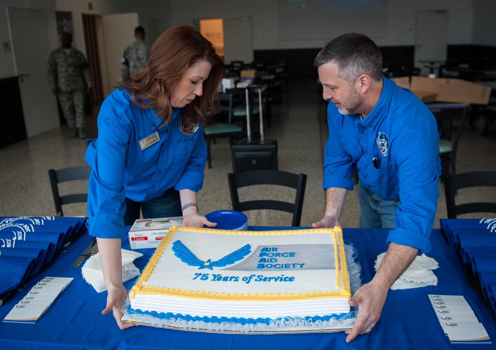 Juli Robertson, 86th Force Support Squadron community readiness specialist, and Wesley Yancey, 86th Force Support Squadron exceptional family member program and family support specialist, sit a cake down on a booth celebrating the Air Force Aid Society’s 75th anniversary on Ramstein Air Base, Germany, Mar. 10, 2017. Celebrations were held at the Kaiserslautern Military Community Center for families to come together in a large forum, and the event reminded people of the many different ways the AFAS helps Airmen and their families. (U.S. Air Force photo by Senior Airman Lane T. Plummer)