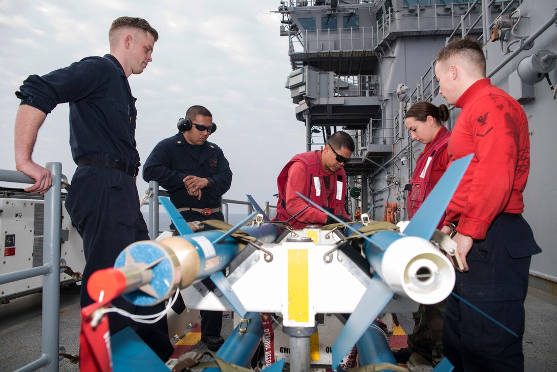 Navy Chiefs Oliver Christofferson, in red vest and sunglasses, and Rich Delgado, center left, train Petty Officers 3rd Class Ian Callahan, left, Austin Hoffman, right, and Ciara Poder on how to prepare laser guided training bombs on the flight deck of the amphibious assault ship USS Bonhomme Richard in the Philippine Sea, March 10, 2017. Navy photo by Seaman Jesse Marquez Magallanes