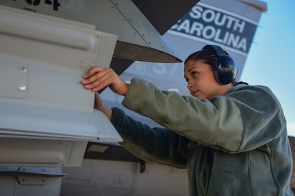 U.S. Air Force Senior Airman Sydney Byrd, 169th Aircraft Maintenance Squadron weapons loader, assists in affixing a bomb onto the wing of an F-16 Fighting Falcon fighter jet on the taxiway at McEntire Joint National Guard Base, South Carolina, Nov. 22, 2016. 