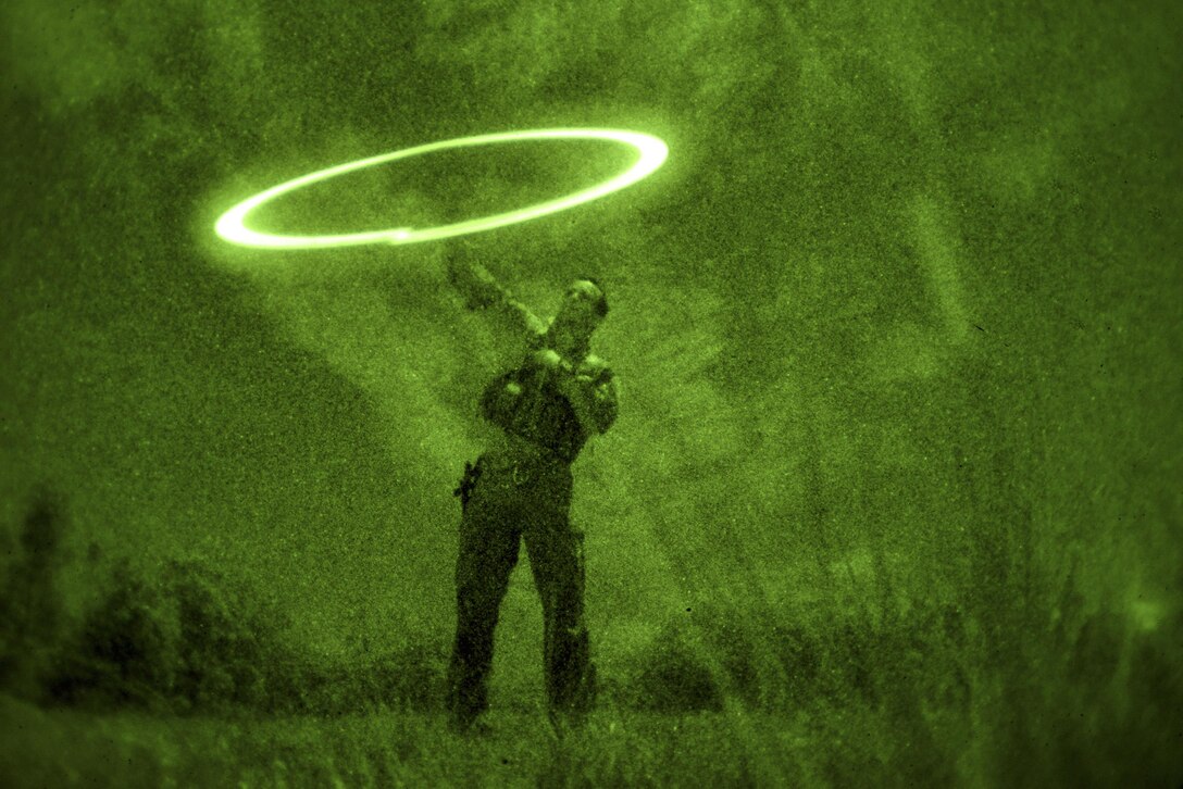 As seen through a night-vision device, Air Force Senior Airman Jonathan Harvey demonstrates how to contact friendly forces during survival training at the Army's Jungle Operations Training Course in Hawaii, March 8, 2017. Harvey is a survival, evasion, resistance and escape specialist assigned to the 106th Rescue Wing. Air National Guard photo by Staff Sgt. Christopher S. Muncy