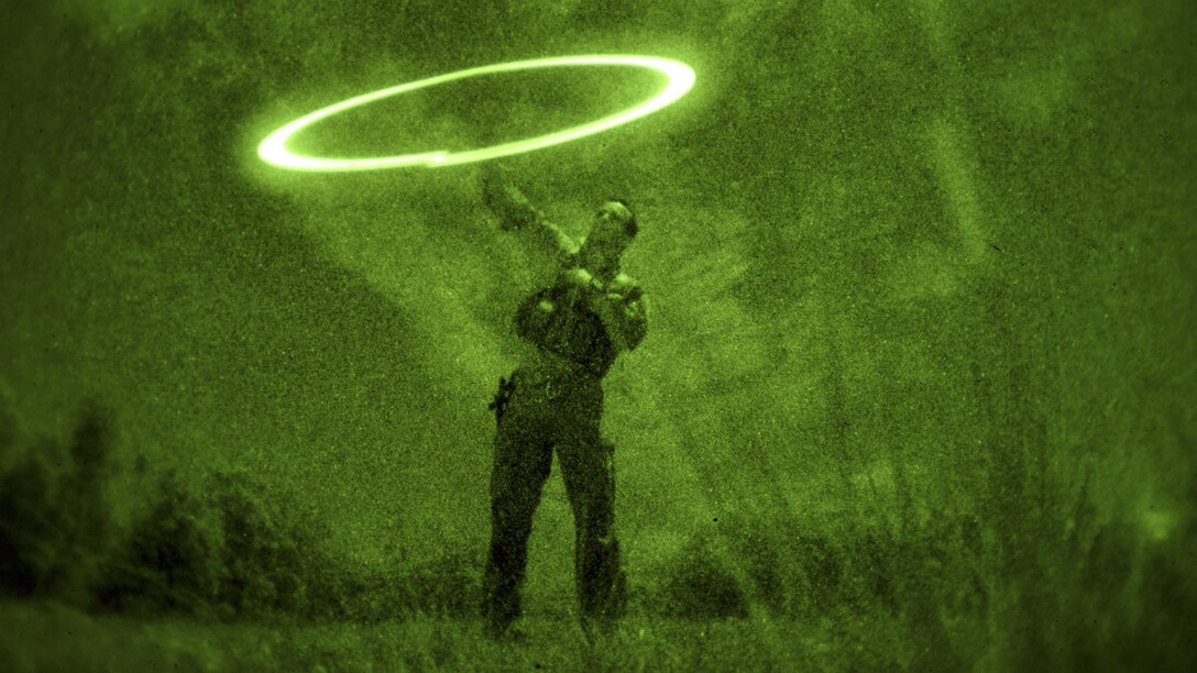 As seen through a night-vision device, Air Force Senior Airman Jonathan Harvey demonstrates how to contact friendly forces during survival training at the Army's Jungle Operations Training Course in Hawaii, March 8, 2017. Harvey is a survival, evasion, resistance and escape specialist assigned to the 106th Rescue Wing. Air National Guard photo by Staff Sgt. Christopher S. Muncy