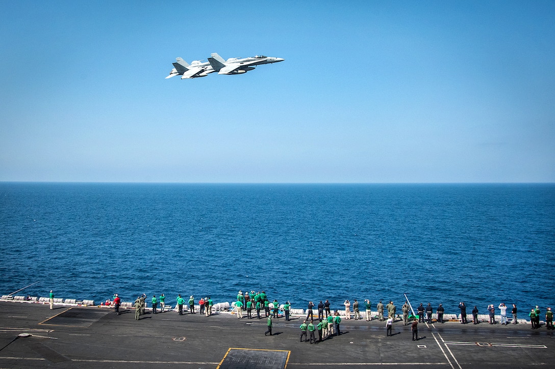 Two F/A-18C Hornets fly above the aircraft carrier USS Carl Vinson, during an in-flight change of command in the South China Sea, March 6, 2017. The pilots are assigned to Strike Fighter Squadron 34. Navy photo by Petty Officer 3rd Class Matt Brown