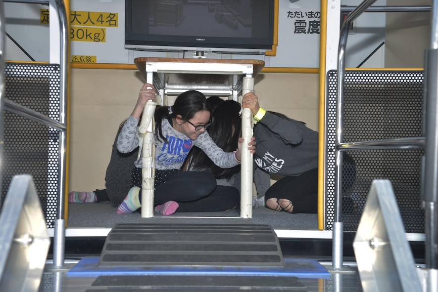 Yokota personnel sit under a table in an earthquake simulator during the Yokota Safety and Readiness Festival at Yokota Air Base, Japan, March 10, 2017. The event allowed Yokota personnel to have fun while learning how to safely handle situations that could take place in their daily lives. (U.S. Air Force photo by Staff Sgt. David Owsianka)