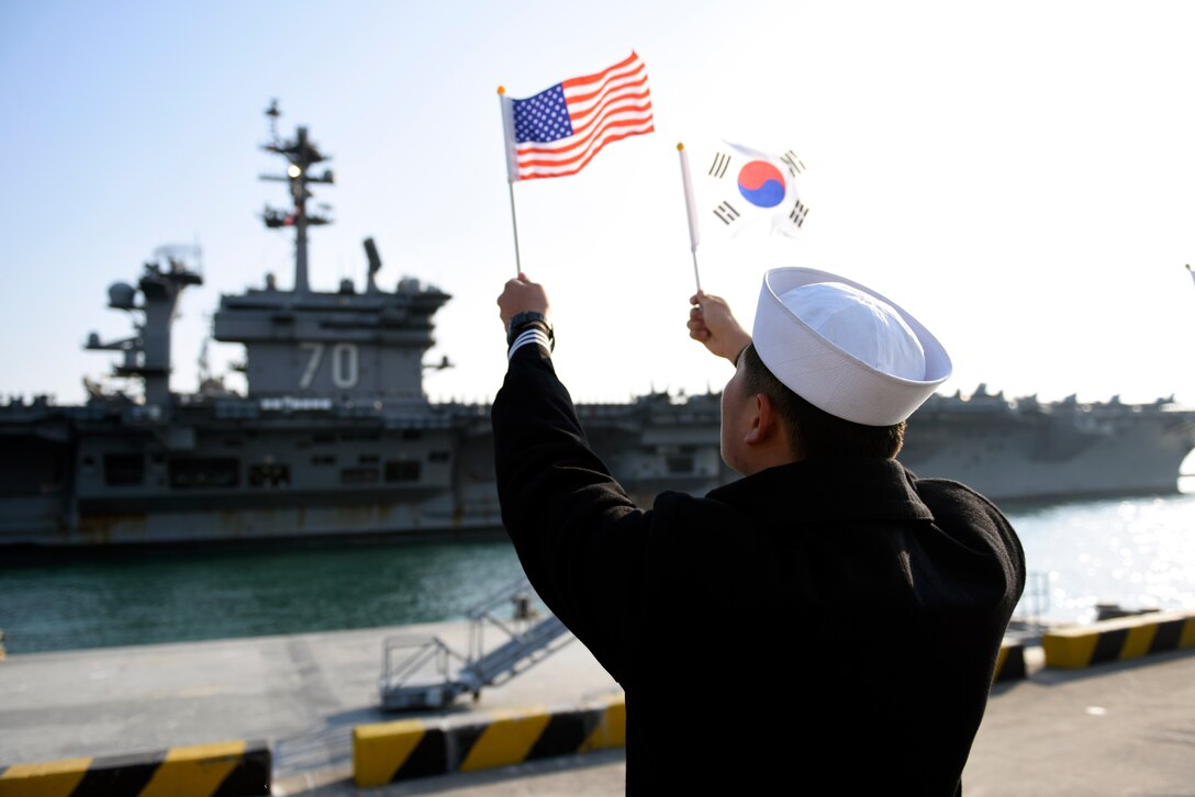 A Republic of Korea (ROK) sailor waves flags as Nimitz-class aircraft carrier USS Carl Vinson (CVN-70) pulls into ROK Fleet headquarters. The Carl Vinson Carrier Strike Group is on a regularly scheduled Western Pacific deployment as part of the U.S. Pacific Fleet-led initiative to extend the command and control functions of U.S. 3rd Fleet. 