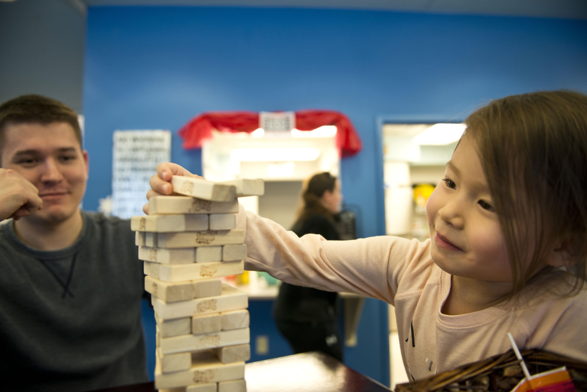 Air Force Staff Sgt. Jacob Garrison, 354th Operations Group, Detachment 1 personal security manager watches his daughter Kaelyn as she pulls a block out of a Jenga tower in the United Service Organization on Joint Base Elmendorf-Richardson, Alaska, March 10. Garrison and his family helped plan and execute a mentorship event at the USO where noncommissioned officers reached out to Airmen in an environment free of rank and time constraints.