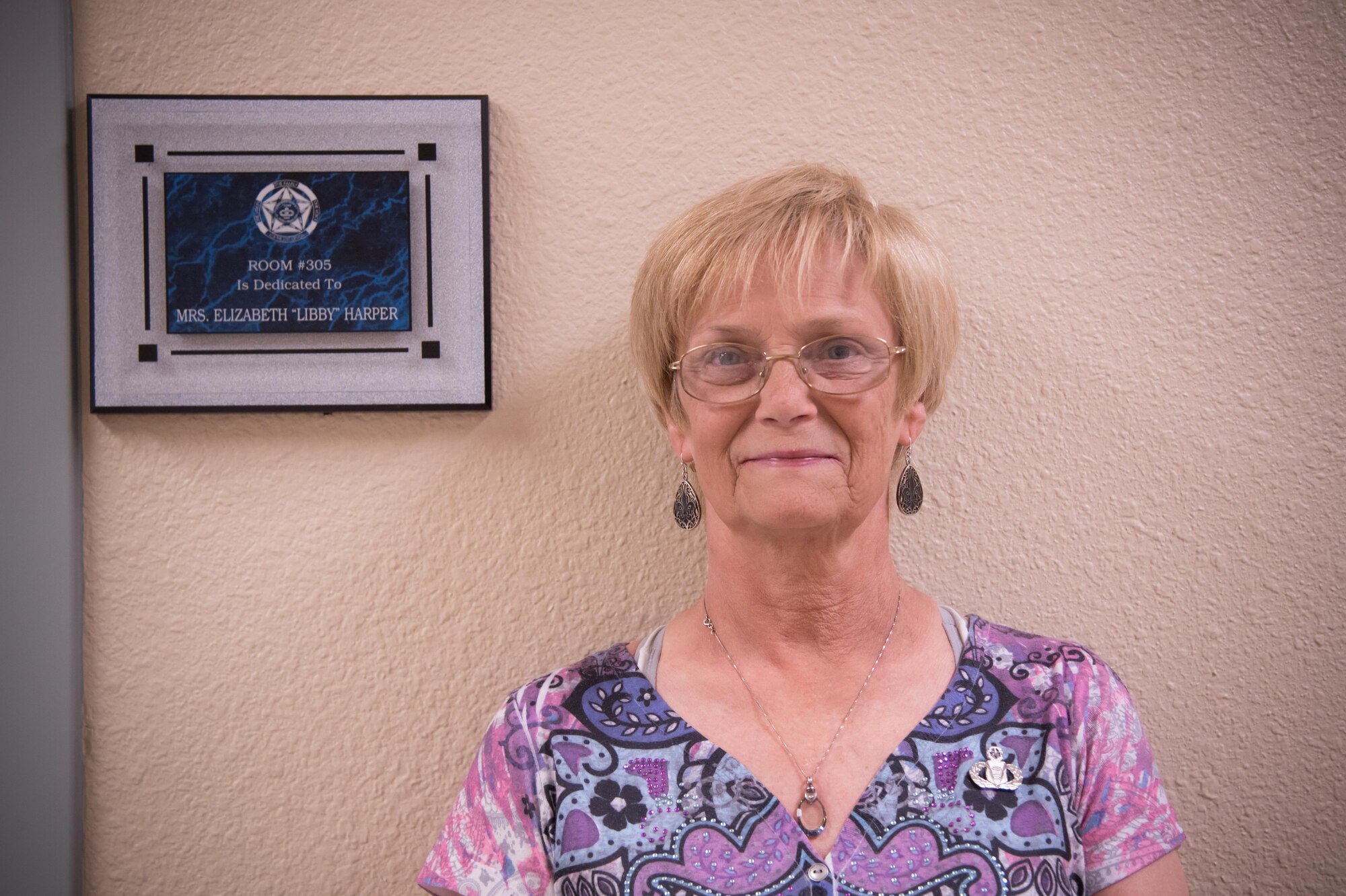 Libby Harper, 81st 81st Operations Support Flight host aviation resource management chief, poses for a photo in front of a plaque that dedicated a room in Cody Hall to her after her retirement ceremony March 3 at Keesler Air Force Base, Mississippi. (U.S. Air Force photo/Staff Sgt. Heather Heiney)