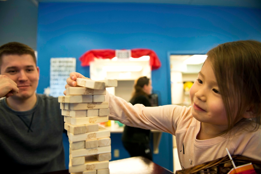 Air Force Staff Sgt. Jacob Garrison watches his daughter, Kaelyn, as she pulls a block from a Jenga tower at Joint Base Elmendorf-Richardson, Alaska, March 10, 2017. Air Force photo by Senior Airman Kyle Johnson