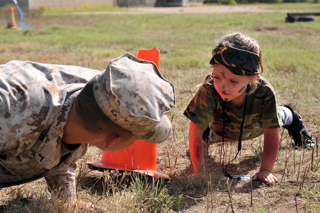 A child performs push-ups with a Marine