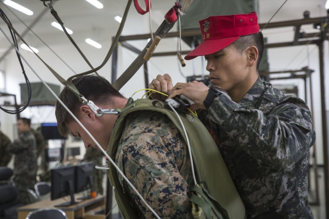 Republic of Korea Marine Corps Master Sgt. Yonhwan Shin helps strap in U.S. Marine Cpl. Justin Morrall to a canopy flight simulator, which allows the Marines to practice steering a parachute canopy, on March 14, 2017, near Camp Mujuk, Republic of Korea. The relationship between ROK and U.S. Marines encompasses the strategic, operational and tactical levels of training. Shin is with 1st Marine Division Parachute Operations Battalion. Morrall, a Denver, Colorado native, is a squad automatic weapon gunner with 3rd Reconnaissance Battalion, 3rd Marine Division, III Marine Expeditionary Force. (U.S. Marine Corps photo by Lance Cpl. Bernadette Wildes) 