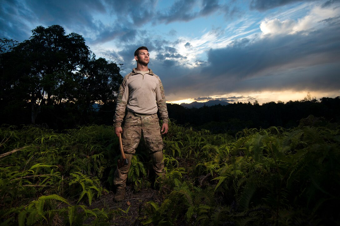 Air Force Senior Airman Alex Triani pauses from chopping wood as the sun sets during survival training at the Army's Jungle Operations Training Course in Hawaii, March 8, 2017. Triani is a survival, evasion, resistance and escape specialist assigned to the 106th Rescue Wing. Air National Guard photo by Staff Sgt. Christopher S. Muncy
