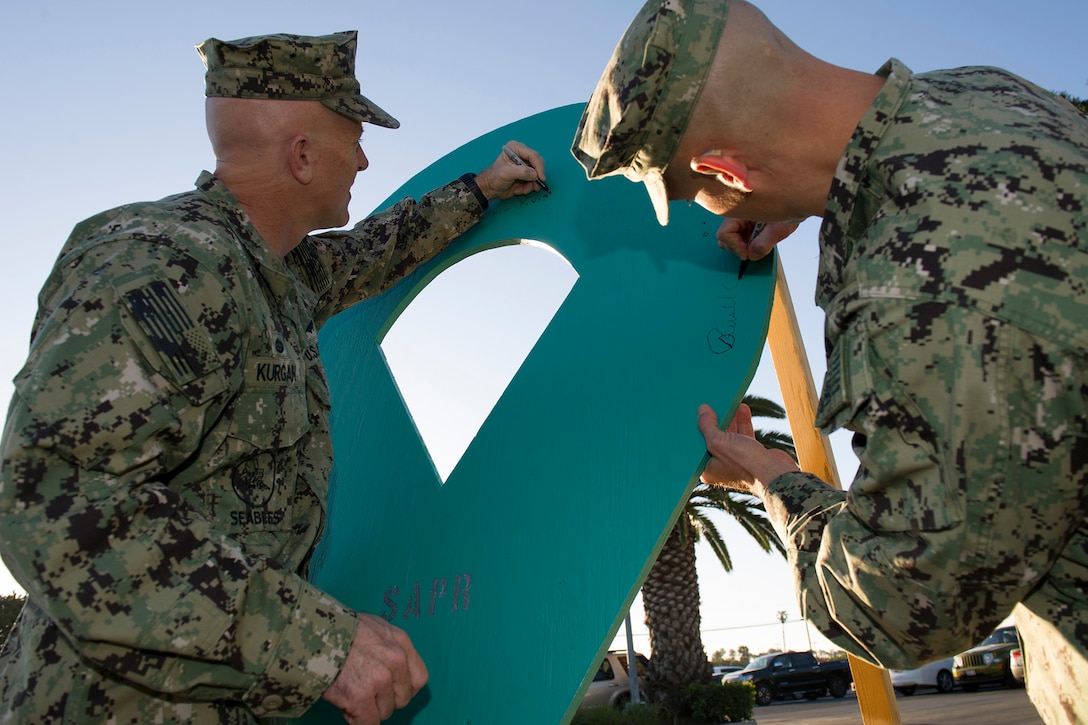 Navy Capt. Christopher Kurgan and Chief Staff Officer Cmdr. Russell Rang sign a Sexual Assault Prevention and Response proclamation board