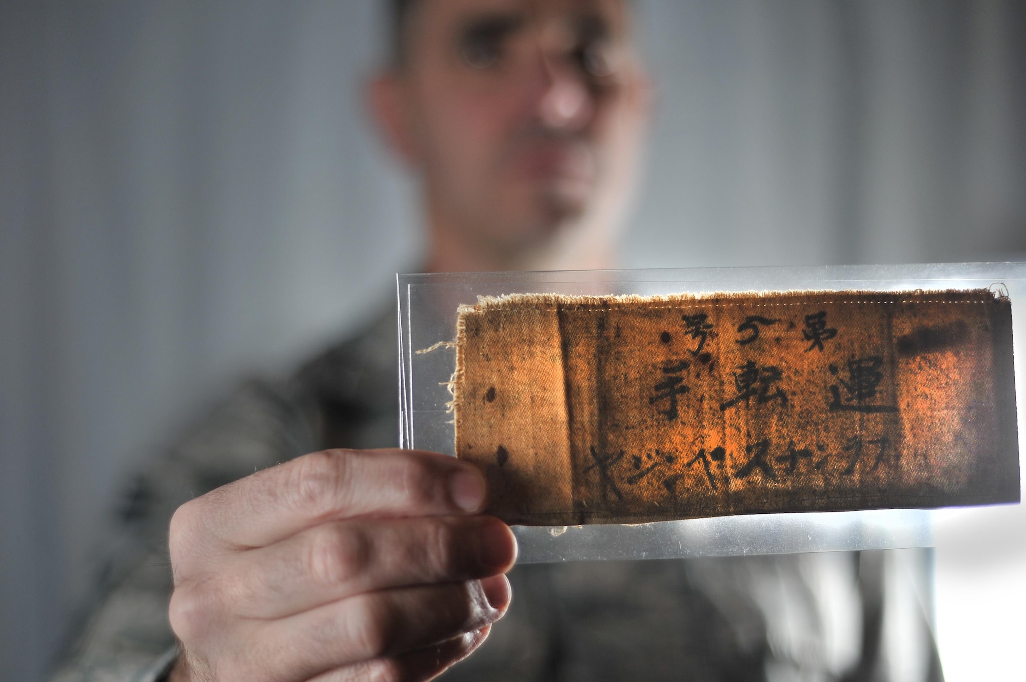 Chief Master Sgt. Jake Higginbotham, 70th Intelligence, Surveillance and Reconnaissance Wing command chief, holds the arm band that Master Sgt. retired Francis M. Bania wore while imprisoned after the Bataan Death March.  (U.S. Air Force photo/Staff Sgt. Alexandre Montes)