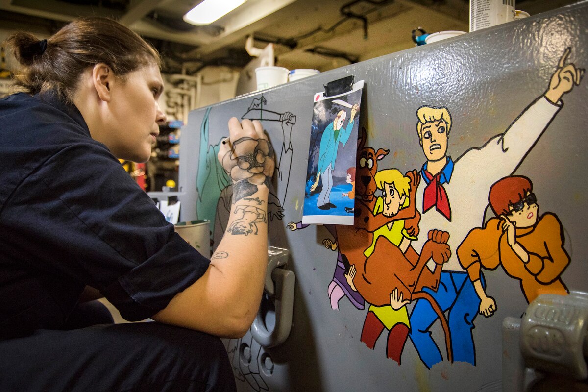 A sailor outlines a design on an aircraft towing tractor on a ship.