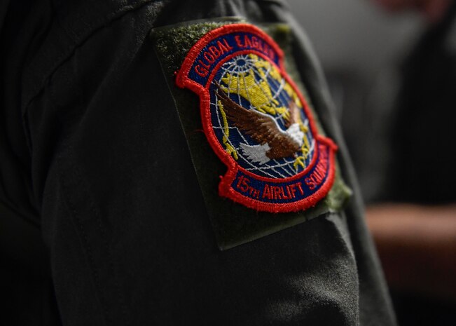 Capt. Jason Carroll, 15th Airlift Squadron airdrop instructor pilot wears the 15th AS patch during a flight to North Auxiliary Airfield in North, South Carolina, March 15, 2017 to execute in-flight training with aircrew eye and respiratory protection system (AERPS) equipment. The flight marked the first time in more than 10 years where aircrews wore AERPS equipment. AERPS equipment consists of a rubber mask, multiple layers of boots and gloves, fan filter system and an audio and speaker system.