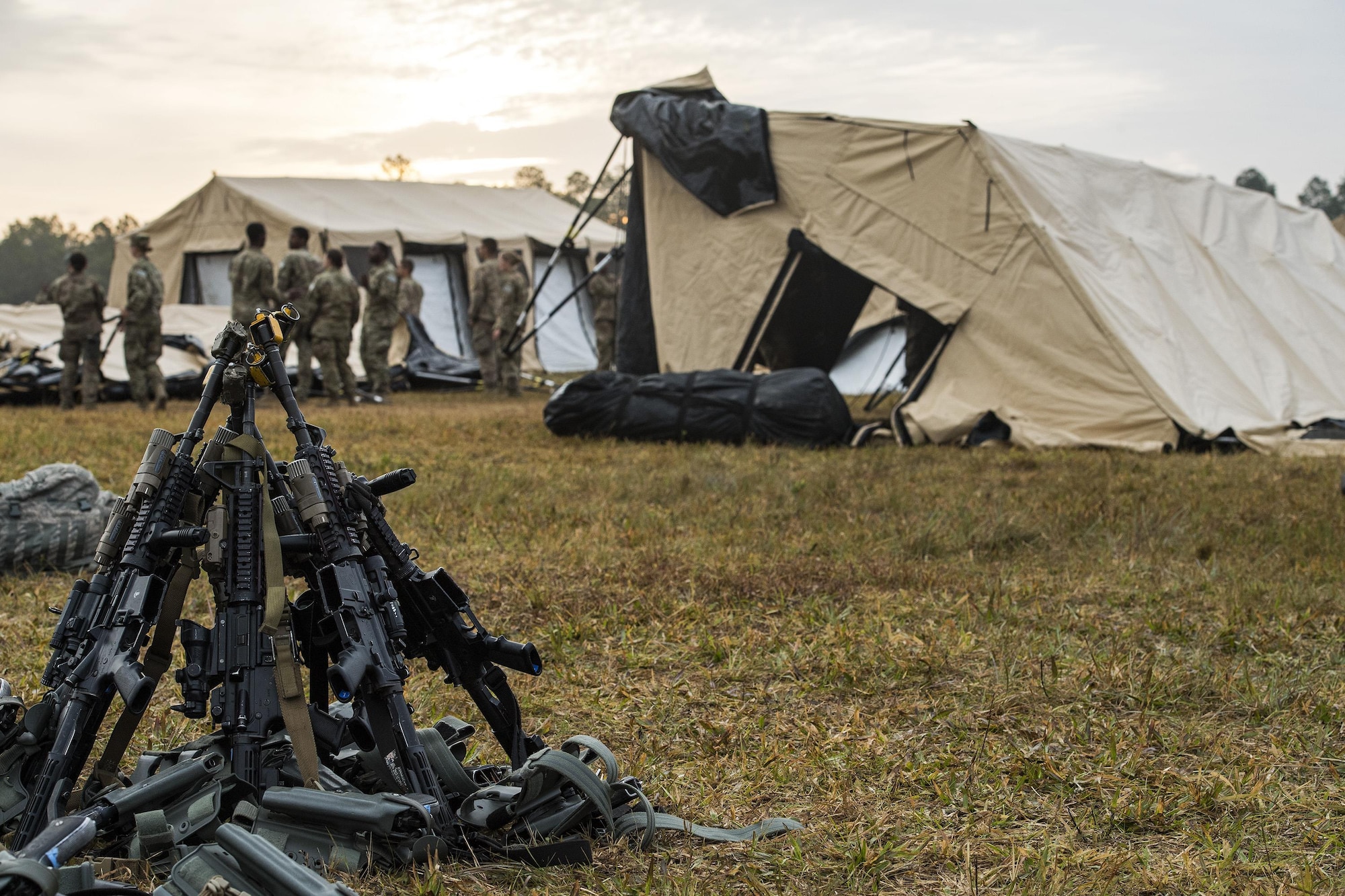 M4 Carbine Rifles rest in a stack while Airmen from the 105th Base Defense Squadron and 822d Base Defense Squadron break down tents at the end of a Mission Readiness Exercise, March 13, 2017, at Avon Park Air Force Range, Fla. Airmen from the 105th BDS embedded into the 822d BDS to participate in the exercise. While the 822d used the exercise to validate their training and regain their status as a Global Response Force, the 105th BDS received training that allowed them to show their capabilities and strengthened the bond between the two squadrons. (U.S. Air Force Photo by Airman 1st Class Janiqua P. Robinson)