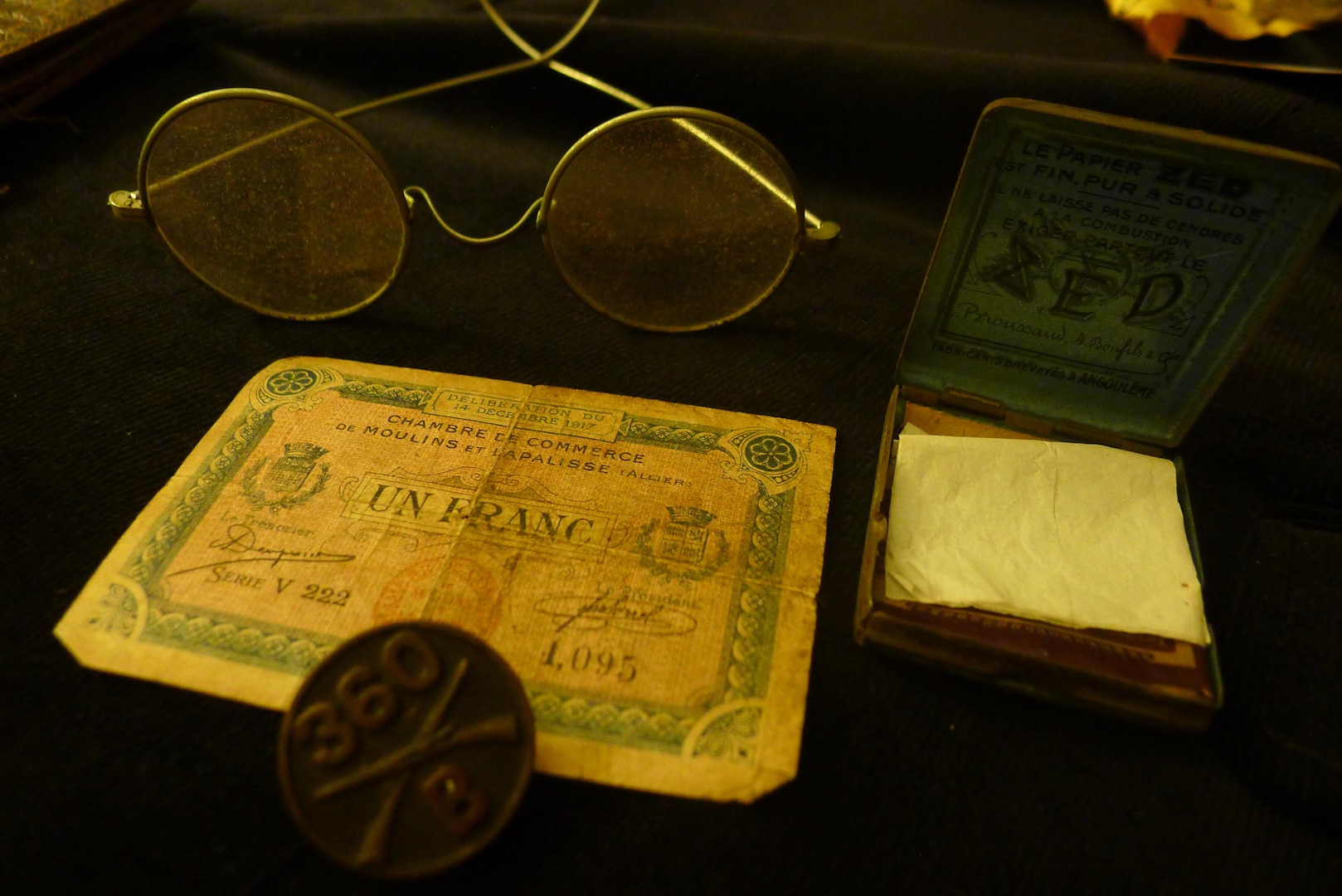 From bottom left: Items Sgt. Leon Bell brought home from WWI include a US Army 360th Infantry button, from his uniform coat; French provisional currency; wire-frame spectacles; and French cigarette rolling papers.