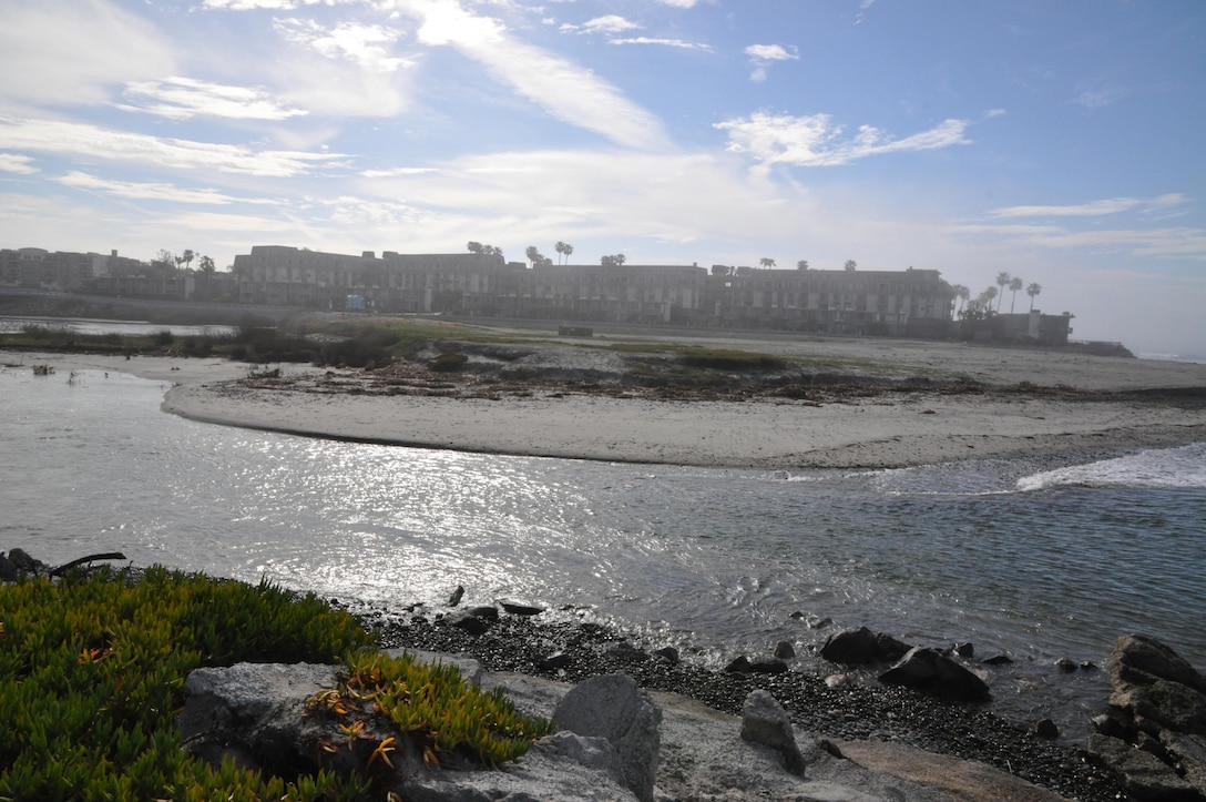 In previous years, sand across the mouth of the San Luis Rey River blocked its connection to the Pacific Ocean,  providing a continuous shoreline. Recent rains have opened the river to the ocean, requiring the contractor to develop a means to span the flowing water in order to replenish the beach to the south.