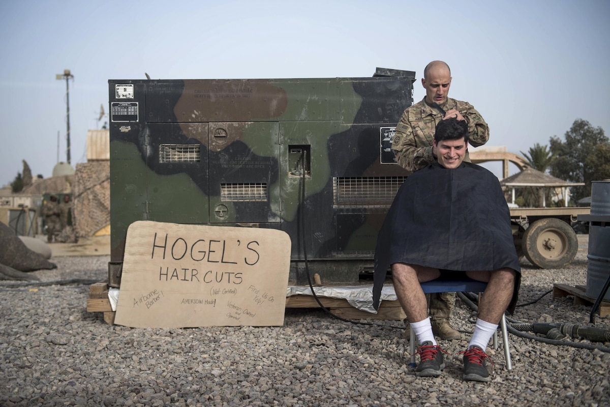 A soldier receives a haircut from another soldier outside.