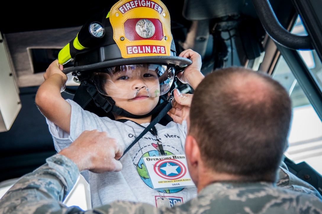 An airman helps a "new recruit" with his fire hat during Operation Hero at Eglin Air Force Base, Fla., Oct. 22, 2017. The mock deployment was created to give military children a glimpse of what their loved ones go through when they leave home. Air Force photo by Samuel King Jr.