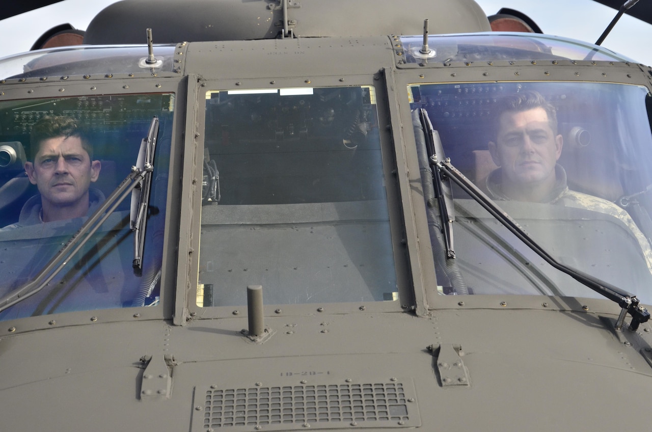 Chief Warrant Officer 4 Justin Larson (Left) and Chief Warrant Officer 5 Noel Larson (Right) pose for a photo in the cockpit of a Black Hawk helicopter they use for their aviation duties Feb. 12, 2017. The two brothers were promoted on the same day at the Aviation Readiness Center on Joint Base Lewis-McChord. (U.S. Army National Guard photo by Sgt. Jodi Eastham)