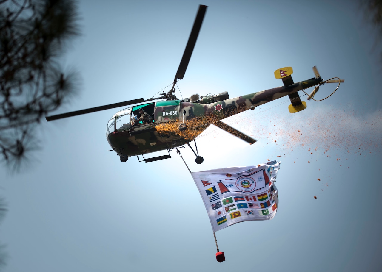 A helicopter does a fly-by dropping flower petals and displaying the banner of all the countries attending exercise Shanti Prayas in Nepal.  Shanti Prayas III is a multinational United Nations peacekeeping exercise designed to provide pre-deployment training to U.N. partner countries in preparation for real-world peacekeeping operations. (U.S. Navy Photo by Petty Officer 2nd Class Taylor Mohr)