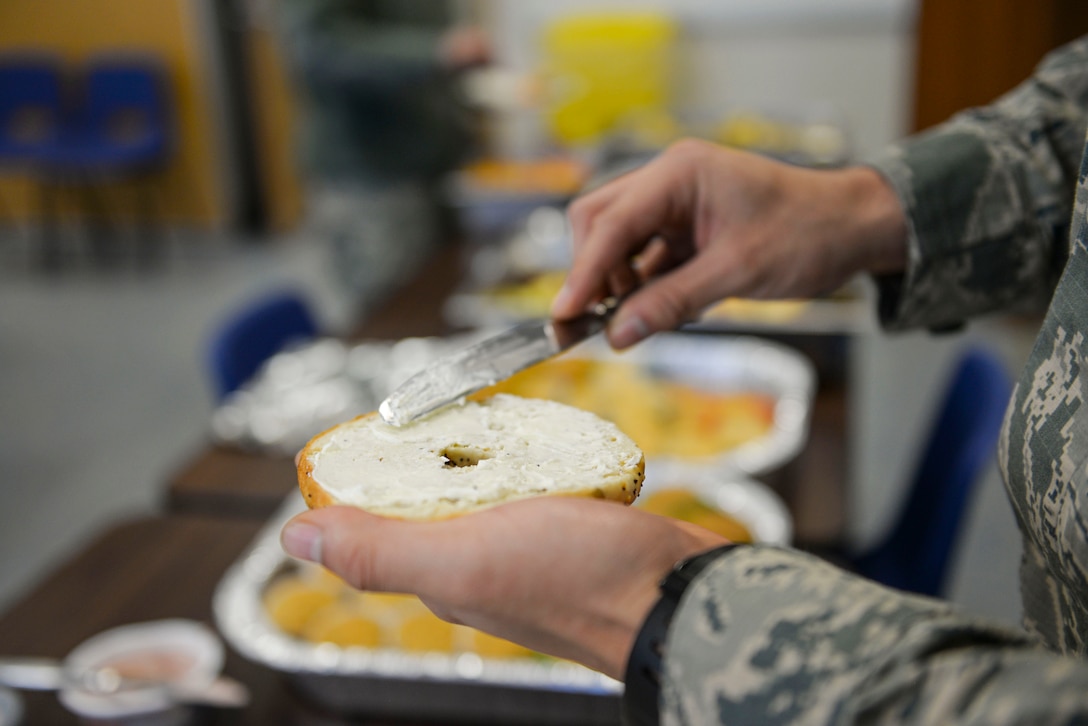 A U.S. Air Force Airmen puts cream cheese on a bagel at the base chapel March 21, 2017, on RAF Mildenhall, England. Airmen in the ranks of airman basic to senior airman were invited to the base chapel to enjoy a free breakfast, compliments of the Airmen Committed to Excellence council. (U.S. Air Force photo by Staff Sgt. Micaiah Anthony)