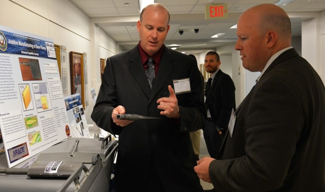 Jake Feeney, an engineer from Marine Corps Systems Command, discusses the additive manufacturing of bow planes with Matthew Walker, a propulsion engineer from Naval Air Warfare Center Weapons Division during the 3-D Print-a-thon hosted by the Navy at the Pentagon on March 15, 2017. (U.S. Navy photo by Kelley Stirling/Released)