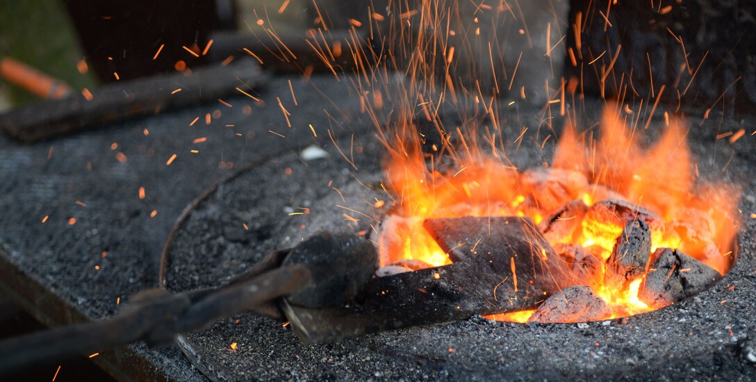 U.S. Air Force Tech. Sgt. Steven Pyott, 100th Security Forces Squadron standards and evaluations sections evaluator and blacksmith, pulls the steel out from the coals Feb. 11, 2017, in Suffolk, England. He uses metal tongs to pull the steel out of the flame so he can work the object into the desired shape. (U.S. Air Force photo by Airman 1st Class Tenley Long)