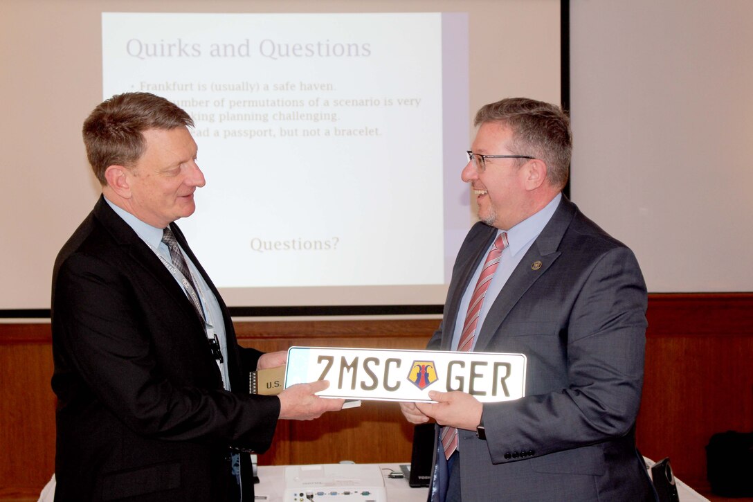 Marshall Derks, of Consular Services at the U.S. Embassy in Frankfurt, accepts a license plate from James Otto, the command executive officer for the 7th Mission Support Command, during the Diplomacy at Work Professional Development Workshop March 22 at the Armstrong Club on Vogelweh Air Force Base. 
