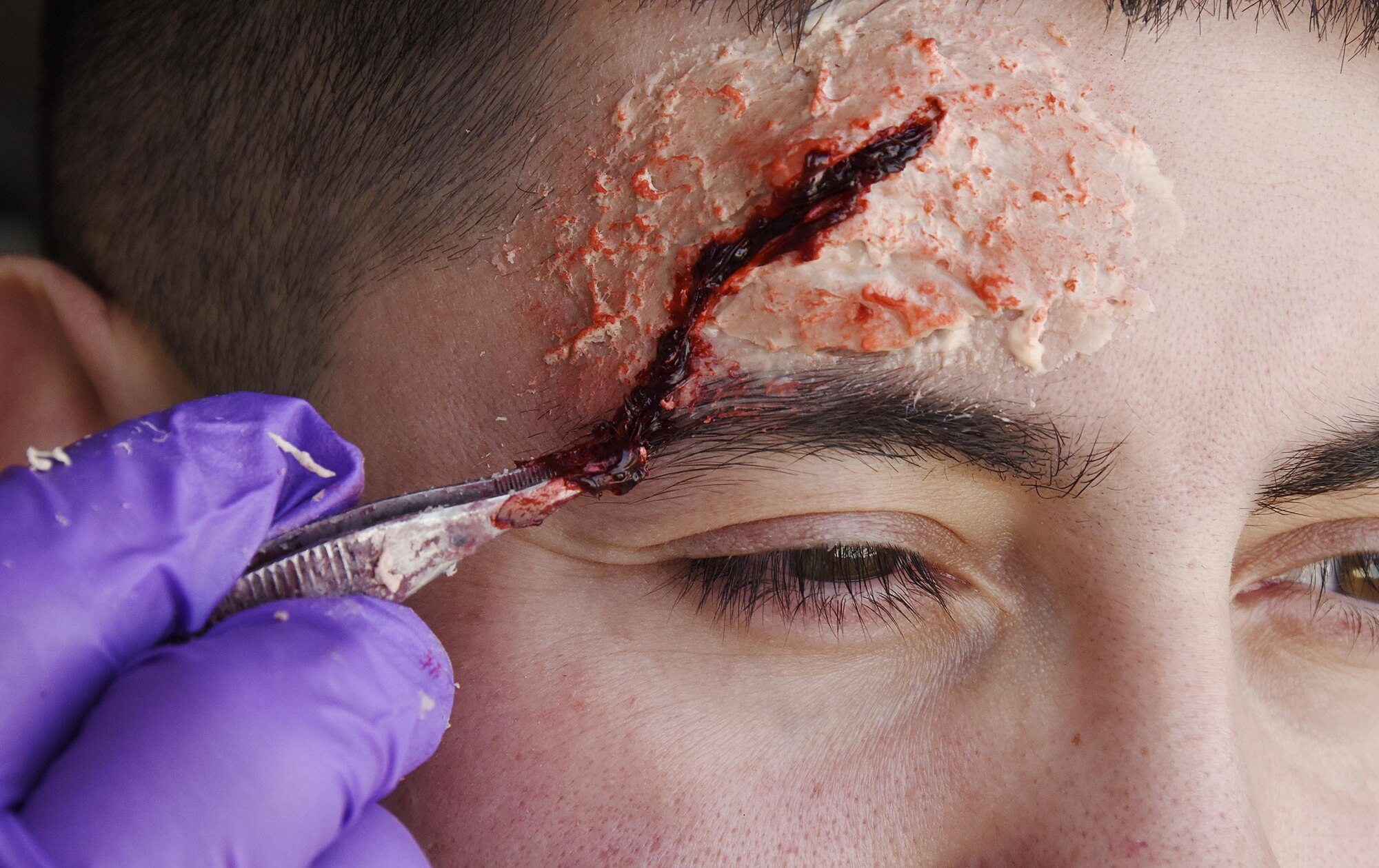 U.S. Air Force Senior Airman Elliseo Trujillo, a bioenvironmental journeyman with the 379th Expeditionary Medical Operations Squadron, sits still as moulage is applied to his face before a Lifeflight medical trauma exercise at Al Udeid Air Base, Qatar, March 21, 2017. Injury specific moulage can be applied to simulate wounds, for example applying dark coloring around the eyes to signify the possibility of head trauma. This training endeavor was organized in the hopes of bringing synergy in capabilities between medical responders at Al Udeid AB, running through every echelon of care a live patient would encounter. (U.S. Air Force photo by Senior Airman Cynthia A. Innocenti)