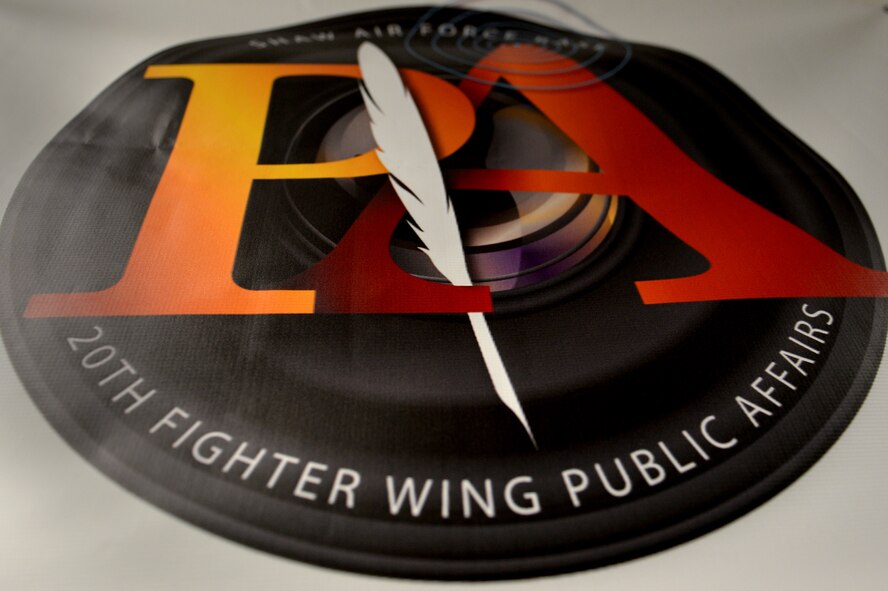 The 20th Fighter Wing (FW) Public Affairs (PA) logo hangs in the public affairs office at Shaw Air Force Base, S.C., March 21, 2017. The public affairs career field is tasked with providing trusted counsel to leaders as well as building, maintaining and strengthening Airmen morale and readiness. These tasks are accomplished by showcasing base-wide activities through still-photography and videography, media escorting and maintaining positive relationships with the local community and media outlets. (U.S. Air Force photo by Airman 1st Class Christopher Maldonado) 