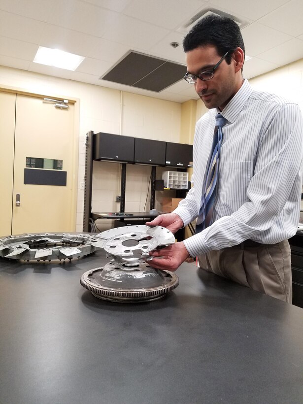 AFRL materials engineer Alan Oquendo demonstrates the failed flywheel assembly and engine cooling fan that resulted in a non-injury incident involving the Wright “B” Flyer replica aircraft.  Oquendo and the Materials Integrity team uncovered critical evidence that explained the event and recommend an improved design.  (U.S. Air Force photo/Holly Jordan)