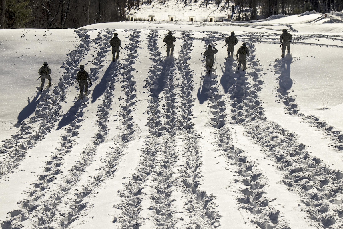 Soldiers trek through snow, leaving long trails.