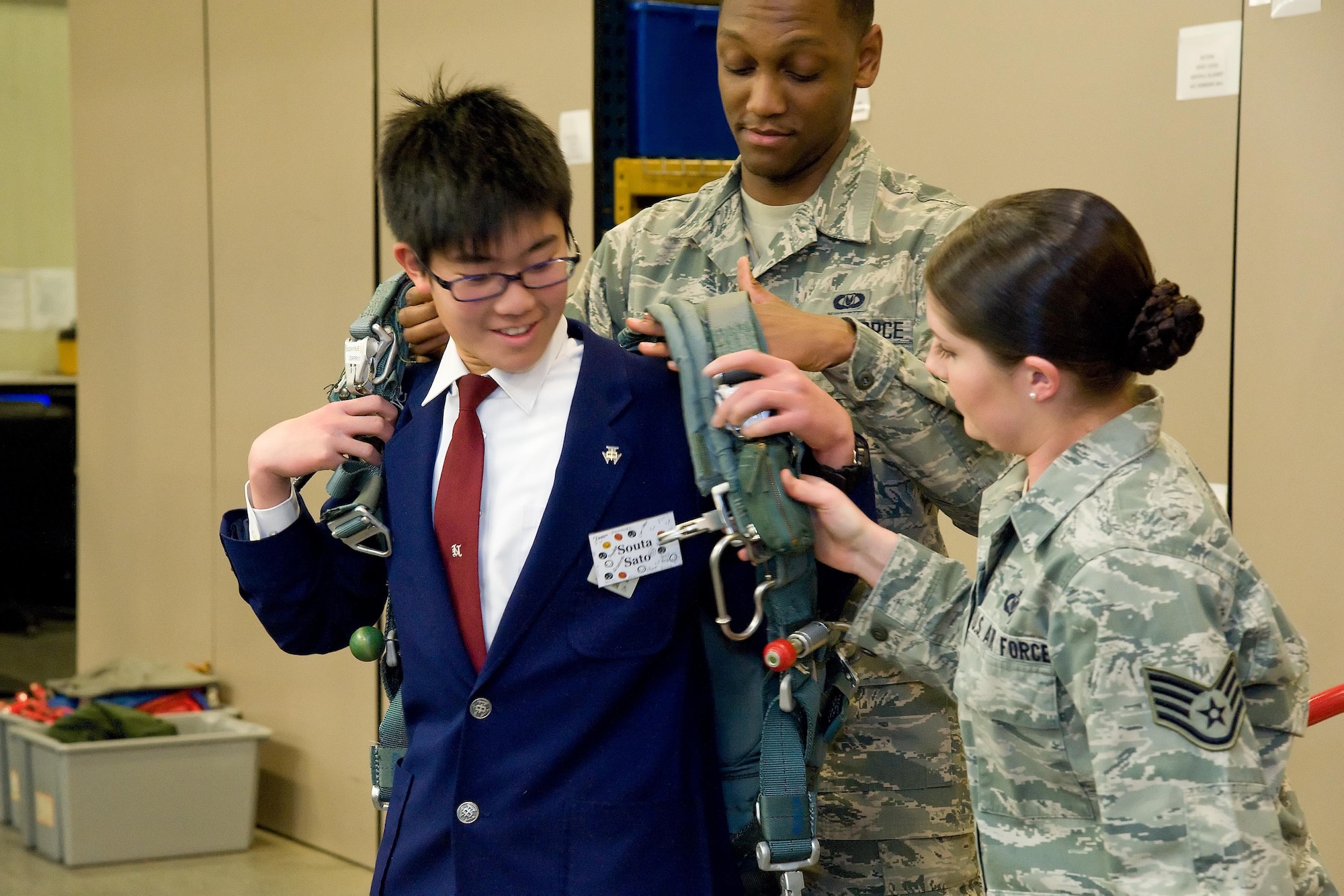 Souta Sato, a junior high school student from the city of Iwanuma, Miyaga Prefecture, Japan, puts on a BA-22 personnel parachute at the 436th Operations Support Squadron's Aircrew Flight Equipment facility March 21, 2017, on Dover Air Force Base, Del. Staff Sgt. Brittany Toth, AFE continuation training instructor, right and Airman 1st Class Andra Johnson, AFE technician, center, provided Sato and 12 other students the opportunity to try on the parachute. (U.S. Air Force photo by Roland Balik)