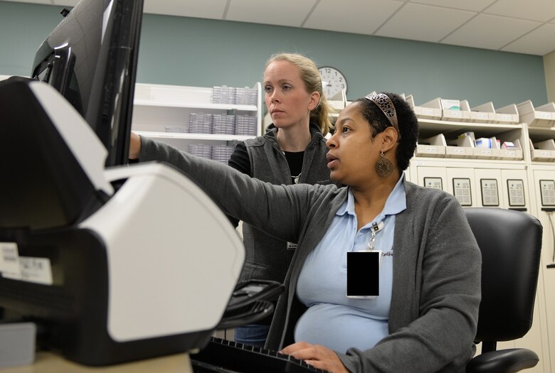 Juliette Zuber, 14th Medical Support Squadron Pharmacy, and Katie Steinback, a student in the Education Center’s pharmacy technician program, discuss day-to-day pharmacy operations March 13, 2017, at Columbus Air Force Base, Mississippi. The new equipment makes learning how to be a pharmacy technician easier due to the user-friendly applications. (U.S. Air Force photo illustration by Airman 1st Class Beaux Hebert)