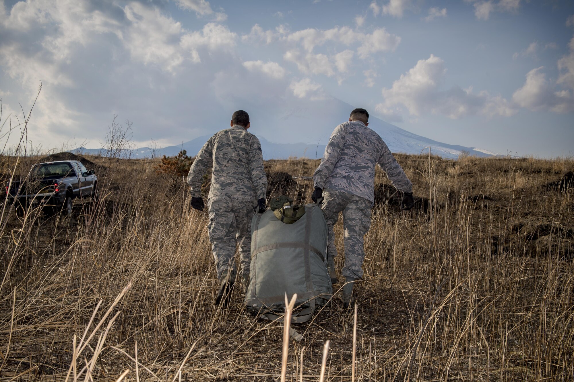 Airmen from the 374th Logistics Readiness Squadron carry a repacked equipment parachute during a cargo drop training exercise March 22, 2017, at Camp Fuji, Japan. From packing the parachutes to recovering them after the drop exercises are complete, the 374 LRS is responsible for every step in building the cargo pallets to ensuring the supplies land safely on the ground. (U.S. Air Force photo by Airman 1st Class Donald Hudson)