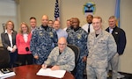 Surrounded by team members, DLA Aviation Commander Air Force Brig. Gen. Allan Day signs the first DLA/Navy retail supply manual on March 24, 2017 at Defense Supply Center Richmond, Virginia.  The manual will lead to improved warfighter support by standardizing policies and processes at DLA Aviation industrial support activities co-located at the Navy's three fleet readiness centers at Cherry Point, North Carolina; San Diego, California and Jacksonville, Florida.