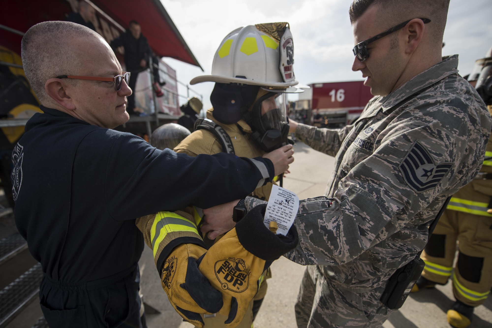 Erwin Colling, 52nd Civil Engineer Squadron station captain, and Tech. Sgt. Jimmy Welch, 52nd Civil Engineer Squadron assistant fire chief of health and safety, assist Chief Master Sgt. Jennifer Brembah, 52nd Mission Support Group chief enlisted manager, with her fire suit before a live fire exercise at Spangdahlem Air Base, Germany, March 23, 2017. MSG leaders were invited to the exercise where they received firefighting experience by practicing hose advancement and extinguishing techniques. (U.S. Air Force photo by Airman 1st Class Preston Cherry)