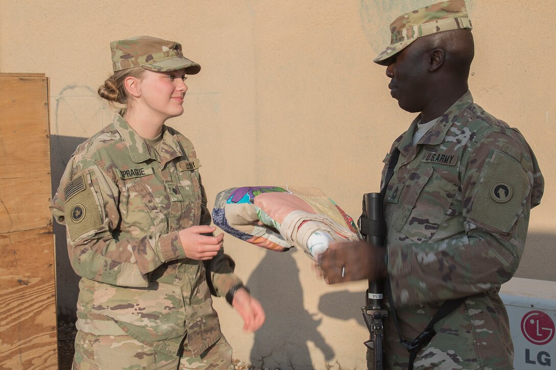 Army Master Sgt. Samuel W. Gilpin, a chaplain assistant with the 1st Sustainment Command Unit Ministry Team, presents a quilt to Spc. Zowie Sprague, a chaplain assistant with the 314th Combat Sustainment Support Battalion Unit Ministry Team during a battlefield circulation visit in Taji, Iraq, Feb. 14, 2017. The quilt was hand-made by a family from a small town in Texas. Army photo by Sgt. Cesar E. Leon