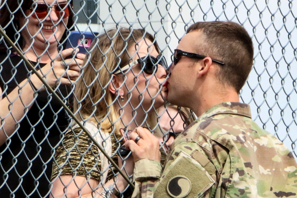 A National Guardsman shares a kiss with a woman with a fence between them.