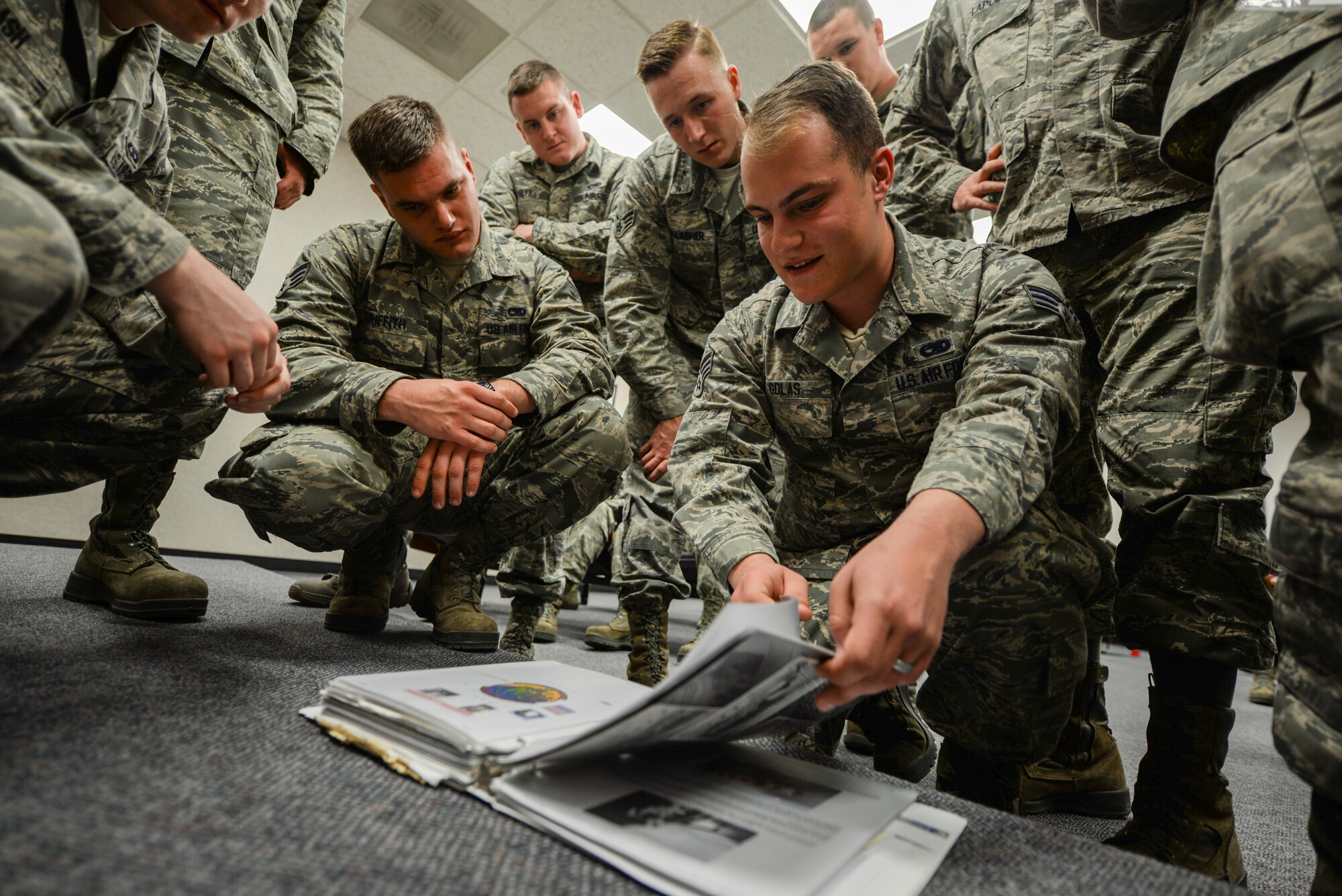 Airmen huddle around a binder full of Air Force heritage pictures and stories inside the Airman Leadership School at Ellsworth Air Force Base, S.D., March 20, 2017. During a presentation by Robert Schilling, a former Airman and gunner on the AC-47 “Spooky” during the Vietnam War, students were able to flip through a binder of information about the aircraft, its crew and what they accomplished. (U.S. Air Force photo by Airman 1st Class Randahl J. Jenson) 