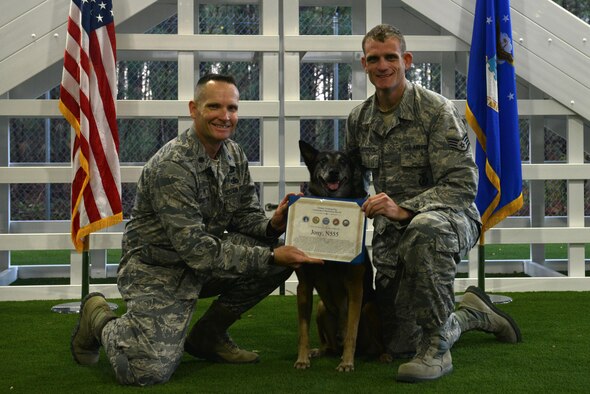 Lt. Col. Garon Shelton, the 20th Security Forces Squadron commander, awards Jony, a retiring 20th SFS military working dog, a certificate of meritorious service, while Staff Sgt. Brian Claypool, a 20th SFS MWD handler, holds the certificate at Shaw Air Force Base, S.C., March 22, 2017. Jony retired after nine years of service due to a compressed disc in his spine. (U.S. Air Force photo/Airman 1st Class Destinee Sweeney)