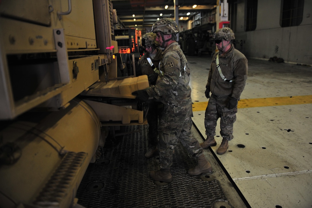 Spc. Michael Mustard, Spc. Stephanie Van Ommen, and Spc. Alex Stamm, all motor transport operators, 32nd Composite Truck Company, 4th Sustainment Brigade, 4th Infantry Division, prepare a heavy equipment transporter to drive off a cargo ship at Gdansk, Poland, March 28. The Soldiers are part of one of 17 active duty, U.S. Army Reserve and national guard units arriving to Poland to support Atlantic Resolve under the 16th Sustainment Brigade.  (U.S. Army photo by Sgt. 1st Class Jacob A. McDonald, 21st Theater Sustainment Command Public Affairs)